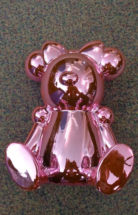 A CERAMIC EARTHENWARE MONEY BOX IN THE FORM OF A MOUSE. IT HAS A SHINY PINK ELECTROPLATE APPEARANCE, AND STANDS ABOUT 21 CENTIMETRES HIGH. THERE IS A COIN SLOT ON THE BACK OF THE HEAD AND A RUBBER STOPPER COVERING A HOLE AT THE BOTTOM.