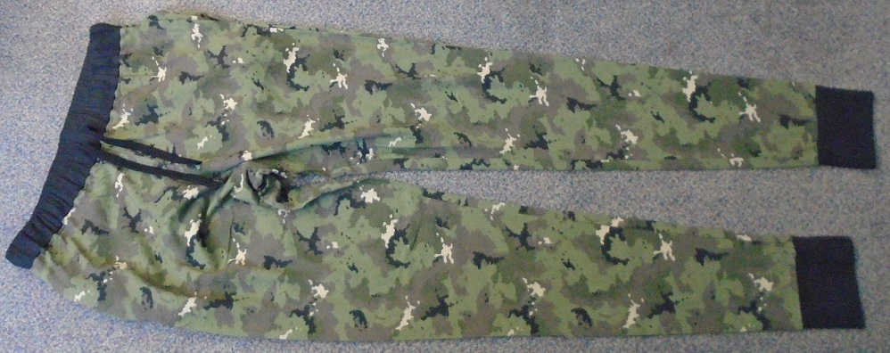 LOUNGEWEAR KNITTED TROUSERS, MADE OF 100% COTTON. WITH A BLACK ELASTICATED WAISTBAND INCORPORATING A BLACK DRAWSTRING FOR TIGHTENING AROUND THE WAIST, WITHOUT OPENING. THE TROUSERS ENVELOPE EACH LEG SEPARATELY.  AT THE BOTTOM OF EACH LEG IS A WIDE BLACK CUFF. THE TROUSERS HAVE A POCKET IN EACH SIDE NEAR THE TOP OF THE TROUSER. THE TROUSERS INCORPORATE A CAMOUFLAGE STYLE DESIGN IN GREENS, KHAKI, BROWNS AND BLACK. PACKAGED WITH A KNITTED TEE SHIRT CLASSIFIED SEPARATELY.