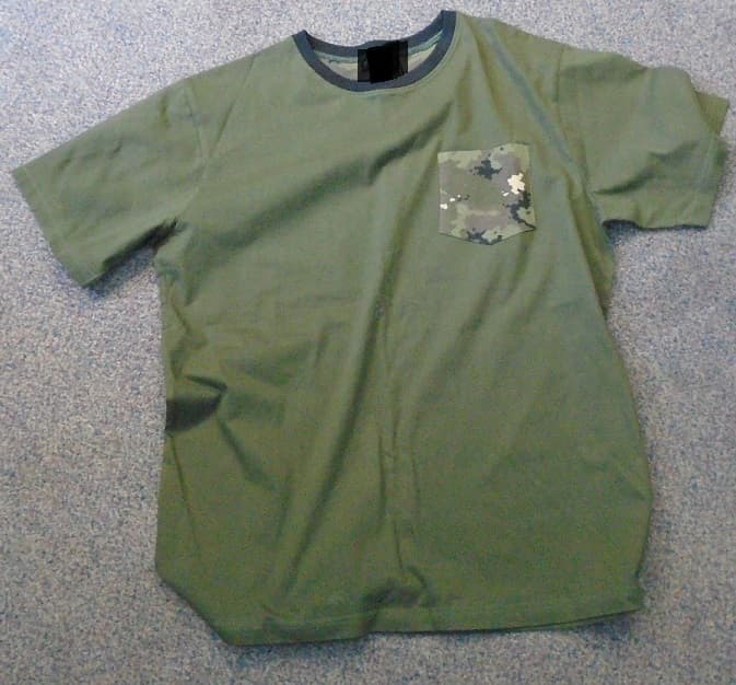 KNITTED TEE SHIRT, MADE OF 100% COTTON. WITH A ROUND NECK AND SHORT SLEEVES. ON THE LEFT BREAST IS A SMALL POCKET MADE OUT OF IDENTICAL CAMOUFLAGE MATERIAL AS THE TROUSER BOTTOMS (CLASSIFIED SEPARATELY). THE TEE SHIRT IS DARK GREEN IN COLOUR WITH A BLACK BAND AROUND THE NECK LINE.