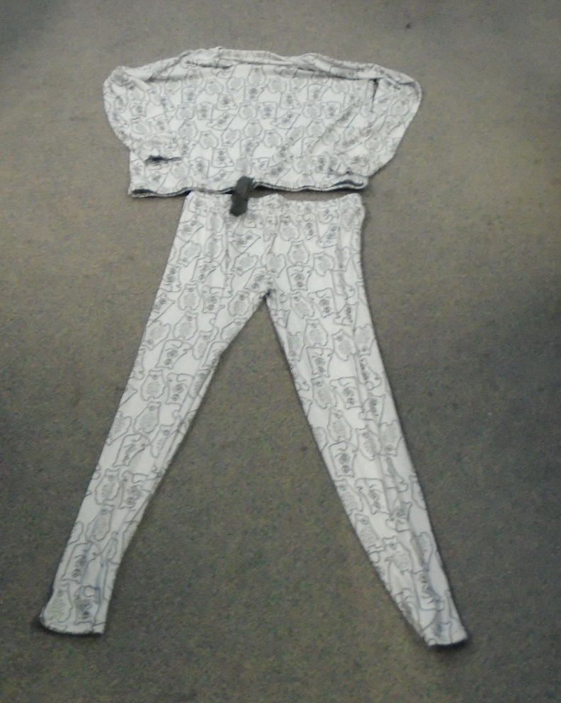 A KNITTED LADIES LOUNGEWEAR ENSEMBLE WITH AN UPPER AND LOWER PART. MADE OF 95% POLYESTER AND 5% ELASTANE. THE TOP HAS LONG SLEEVES, A ROUND NECK AND A RIBBON FASTENING ROUND THE BOTTOM. THE BOTTOM PART IS IN THE FORM OF LOOSE FITTING TROUSERS WITH AN ELASTICATED WAIST. BOTH PARTS HAVE THE SAME DESIGN, THIS BEING AN ANIMAL IN BLACK ON A GREY BACKGROUND.