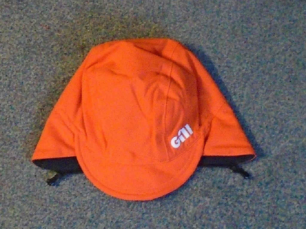 PEAKED CAP STYLE HEADGEAR WITH EXTRA SECTION EXTENDING DOWN AT THE BACK AND SIDES OF THE HEAD.  WITH OUTER SURFACE OF WOVEN WATERPROOF AND BREATHABLE 100% NYLON TEXTILE. LINED WITH 100% POLYESTER  FLEECE TEXTILE. WITH PRINTED LOGO ON SIDE. ORANGE AND BLACK IN COLOUR