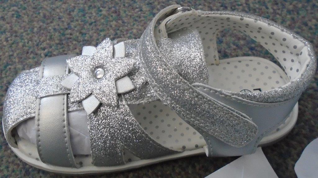 GIRLS SANDAL. WITH UPPERS OF PLASTIC. WITH OUTER SOLES OF PLASTIC. THE VAMP HAS SEVERAL PIECES CUT OUT. WITH VELCRO FASTENING. WITH SOLE AND HEEL COMBINED HAVING A HEIGHT OF LESS THAN 3CM. THE SANDAL IS TWO SHADES OF SILVER,THE ANKLE STRAP AND PART OF THE VAMP HAS A SILVER GLITTER COVERING. THERE IS A DECORATIVE FLOWER ON THE VAMP. THE INSIDE OF THE SANDAL IS CREAM WITH SILVER DOTS. LESS THAN 24CM IN LENGTH.