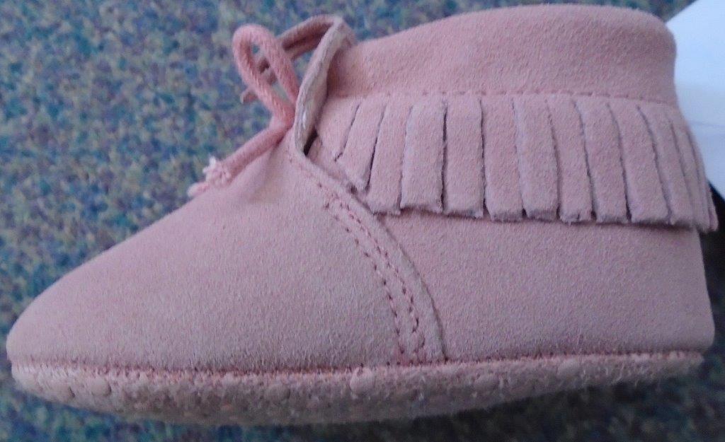 PINK PRAM SHOE FOR BABY GIRLS,COVERING THE ANKLE BUT NO PART OF THE CALF.THE  UPPERS ARE MADE OF LEATHER WITH AN APPLIED SOLE. THE OUTER SOLE IS MADE OF A TEXTILE MATERIAL WITH NON SLIP RUBBER DOTS OF WHICH THE TEXTILE PREDOMINATES.THE SHOES HAVE A KNITTED LINING.THERE IS A BOW  FASTENING AT TOP OF VAMP AND DECORATIVE TASSLES AT THE ANKLE.