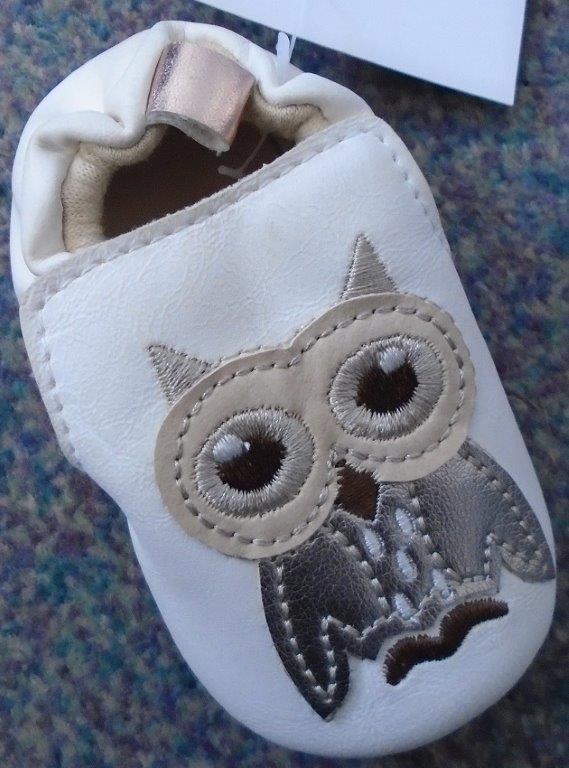 A BABIES ELASTICATED BOOTEE SHOEWITH UPPERS OF PLASTIC WITH AN INNER OF TEXTILE MATERIAL AND AN OUTER SOLE OF TEXTILE WITH PU DOTS FOR GRIP, WITH BRAND INSCRIPTION - TEXTILE PREDOMINANTES. THE SHOE IS CREAM COLOURED WITH AN OWL MOTIF STITCHED TO THE TOP OF THE VAMP. THE SHOE HAS AN INSOLE OF LESS THAN 24CMS IN LENGTH.