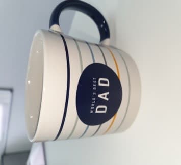 WHITE MUG WITH DARK BLUE HANDLE.MUG IS MADE FROM STONEWARE AND IS APPROXIMATLEY 9CM HIGH AND 9CM WIDE.THIN STRIPES AROUND THE MUG IN BLUES, GREEN AND YELLOW. BLUE CIRCLE IN MIDDLE WITH THE SLOGAN WORLDS BEST DAD IN WHITE IN THE CENTRE.