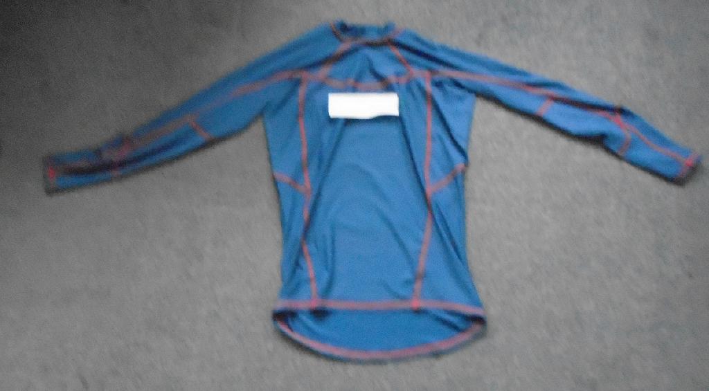 A KNITTED LONG SLEEVE T-SHIRT FOR UNISEX. REACHING DOWN TO BELOW THE WAIST. WITH A ROUND NECK WITHOUT AN OPENING OR FASTENING. WITH A 3CM DEEP BAND AROUND THE NECKLINE. HEMMED AT THE SLEEVE ENDS AND AT THE BASE OF GARMENT. 4 WAY STRETCH FABRIC. WITH FLATLOCKED SEAMS FOR COMFORT. WITH A PRINTED COMPANY LOGO IN THE MIDDLE OF THE CHEST, AND WORDING ACROSS THE REAR LEFT SHOULDER SEAM. THE T-SHIRT IS MADE OF 86% POLYESTER AND 14% ELASTANE. OCEAN BLUE IN COLOUR WITH RED FLATLOCKED STITCHED SEAMS. PACKAGED IN A CLEAR PLASTIC BAG WITH A PRINTED BARCODE, GARMENT DESCRIPTION, PRODUCT CODE AND SIZE.