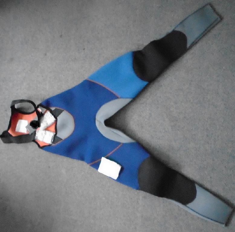 A UNISEX ALL IN ONE GARMENT WITHOUT SLEEVES DESIGNED FOR WATER SPORTS. MADE OF NON CELLULAR NEOPRENE RUBBER COVERED ON BOTH SURFACES WITH A KNITTED NYLON TEXTILE. REACHING FROM THE SHOULDERS TO THE ANKLES ENVELOPING EACH LEG SEPARATELY. WITH A BIB AT THE BACK AND ELASTICATED ADJUSTABLE STRAPS EXTENDING FROM THE SHOULDERS TO THE FRONT OF THE WAIST, WITH SIDE RELEASE BUCKLES. ON THE THIGH AREA OF THE REAR OF THE GARMENT ARE EXTERNALLY FIXED HIKING PADS WITH REINFORCED BATTENS MADE OF FIBRE GLASS WITH AN OUTER SURFACE COVERING OF 100% NYLON POLYURETHANE COATED. THE KNEE AREA AND BOTTOM AREA HAVE A LAYER OF ABRASION RESISTANT TEXTURED FABRIC ON TOP OF THE NEOPRENE. THE GARMENT IS MADE OF 90% NEOPRENE AND 10% NYLON. THERE IS A COMPANY LOGO ON THE RIGHT THIGH TO THE OUTER SIDE.  WITH A FURTHER THREE SMALL SYMBOLS TO THE BOTTOM LEFT SIDE LEG (A SET OF 4 SQUARES, A THERMOMETER AND 4 SMALL ARROWS). PACKAGED IN A CLEAR PLASTIC BAG WITH A PRINTED BARCODE, GARMENT DESCRIPTION, PRODUCT CODE AND SIZE.