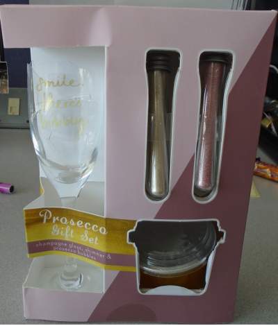 A SINGLE STEM FLUTE GLASS MEASURING APPROXIMATELY 20 CM IN HEIGHT.THE WORDS 'SMILE THERES BUBBLY ' HAS BEEN PRINTED ON THE FRONT. PACKAGED WITH TWO SIX GRAM GLASS TUBES  OF FLAVOURED POWDER AND A PLASTIC JAR OF ORANGE FLAVOUR BUBBLES IN A PRESENTATION BOX.PUT UP FOR RETAIL SALE
PINK PROSECCO SHIMMER INGREDIENTS: SUGAR, ACIDITY REGULATOR,THICKENER,FLAVOURINGS ANTI CAKING AGENT.
WHITE LYCHEE SHIMMER INGREDIENTS:SUGAR,ACIDITY REGULATOR,THICKENER ,ANTI CAKING AGENT,FLAVOURINGS,COLOUR , SWEETENER.
ORANGE FLAVOUR BUBBLES:WATER,SUGAR,GLUCOSE,APPLE JUICE,THICKENING AGENT,ACIDITY REGULATOR,EMULSIFIER,FLAVOURNG,PRESERVATIVE,COLOUR,SWEETENER.
