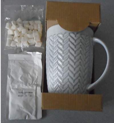 A STONEWARE MUG WITH HANDLE. MEASURING APPROX 15CM HEIGHT X 10CM WIDTH.  EMBOSSED WITH A HERRINGBONE PATTERN. LIGHT GREY IN COLOUR. PACKAGED WITH MINI MARSHMALLOWS IN A SEALED PLASTIC BAG AND A SEPERATE SACHET OF HOT CHOCOLATE MIX. THE ITEMS ARE PACKAGED TOGETHER FOR RETAIL SALE IN A SHAPED CARDBOARD  SURROUND.
