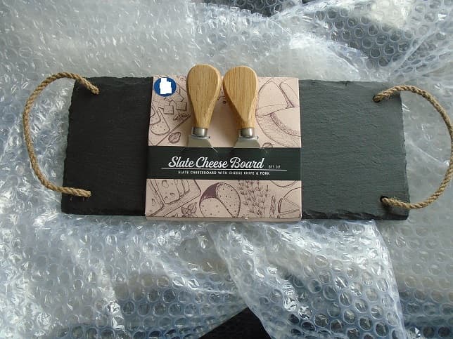 A SLATE CHEESE BOARD WHICH IS APPROXIMATELY 30CM IN LENGTH AND 12CM IN WIDTH. INCLUDED WITH THE SLATE BOARD IS A KNIFE AND FORK FOR CUTTING CHEESE. THE KNIFE AND FORK ARE MADE OF  A RUBBER WOOD HANDLE AND STAINLESS STEEL. IT HAS TWO LOOPS OF TWINE AT WITHER END TO CARRY THE SLATE.

THE ITEMS ARE PUT UP IN A SET FOR RETAIL SALE IN A CARDBOARD SLEEVE.

THE SLATE BOARD IS CONSIDERED TO BE THE ESSENTIAL  CHARACTER IN TERMS OF VALUE AND SCOPE.