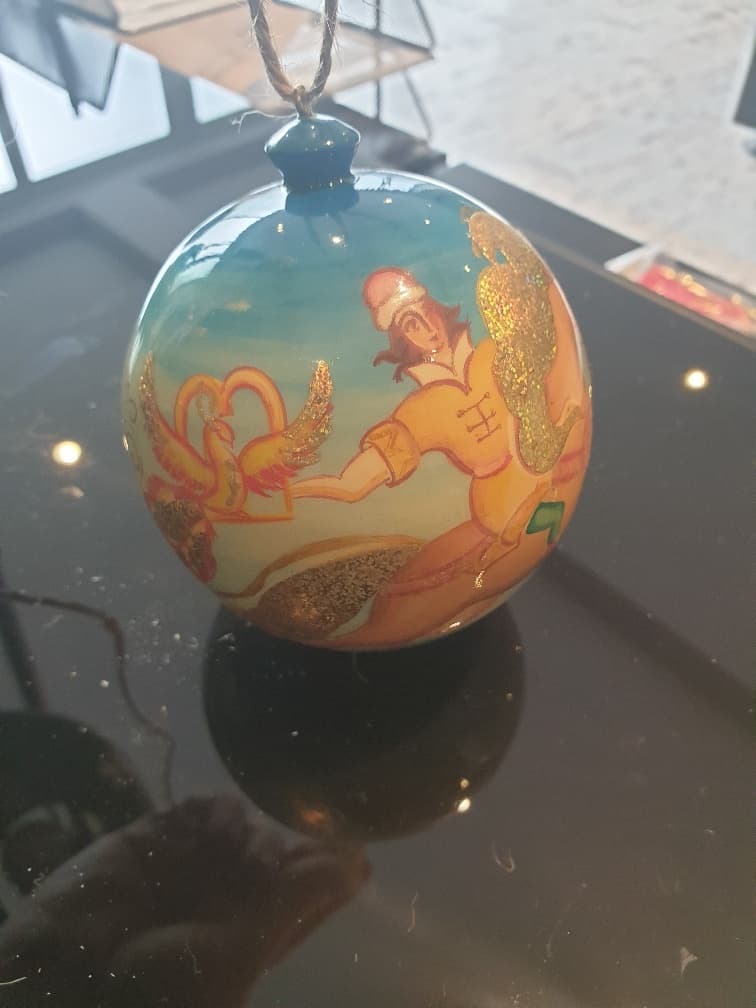 HANGING ORNAMENT MADE OF LINDEN WOOD AND SUSPENDED ON BROWN STRING. IT HAS BEEN LATHE CARVED INTO A BALL SHAPE AND LAQUERED USING SHELLAC AND HAND-PAINTED USING OIL PAINTS.
