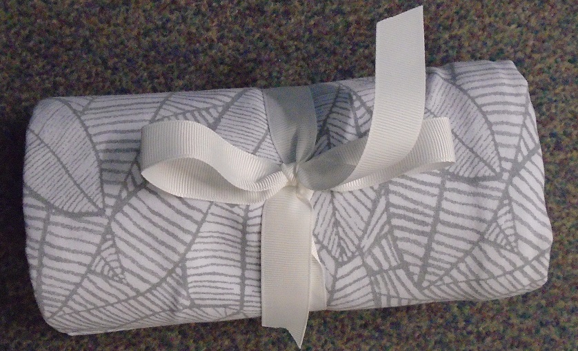 A SINGLE SIDED KNITTED BLANKET PRIMARILY DESIGNED FOR THE USE OF BABIES OR CHILDREN.THE BLANKET IS MADE OF A COTTON AND SPANDEX KNITTED FABRIC. 
COLOURED MID GREY WITH A LIGHT GREY LEAF PATTERN. IT HAS COVERSTITCH FOLDED HEMS ON ALL FOUR SIDES.
THE BLANKET IS DESIGNED FOR SEVERAL USES, E.G., SWADDLING, TO WRAP A BABY/ CHILD. AS A NURSING COVER, AS A BLANKET.
PACKAGED IN A POLYTHENE BAG.