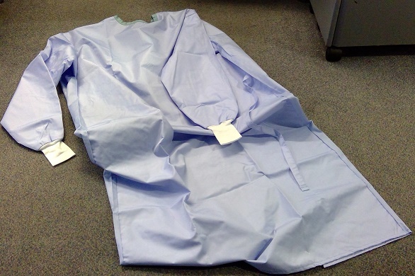 A WOVEN HIGH PROTECTION SURGICAL GOWN FOR UNISEX. MADE OF 99% MICROFIBRE POLYESTER, 1% CARBON. CAN BE USED FOR SURGICAL PROCEDURES WITH HIGH LEVELS OF FLUIDS DUE TO ITS DOUBLE LAYERED FABRIC AT THE FRONT. 
THE GOWN IS LIGHT BLUE IN COLOUR WITH A MINT GREEN NECK COLLAR.  IT HAS LONG SLEEVES WITH A WHITE KNITTED CUFF AT THE BOTTOM OF EACH SLEEVE. 
THE BACK PART OF THE GOWN IS LIGHT BLUE IN COLOUR WITH A BLACK YARN SPACED APPROX EVERY 1CM APART. IT HAS A COMPLETE OPENING AT THE BACK WITH  A TIE BELT FASTENING AND FOUR ADJUSTABLE PRESSTUDS AT THE BACK OF THE COLLAR.