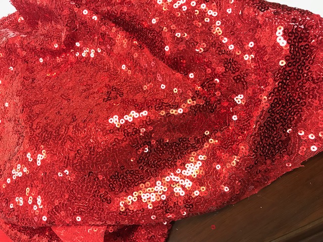 AN EMBROIDERED KNITTED POLYESTER BASE TEXTILE WITH SEQUINS SEWN ONTO THE TOP OF THE FABRIC, HAS A VISIBLE GROUND.  
IT IS A LOOSE FABRIC THAT COMES IN A ROLL. THE VALUE IS LESS THAN 17.50 EURO/KG. CAN BE USED FOR DRESSMAKING OR ARTS & CRAFTS. RED IN COLOUR.