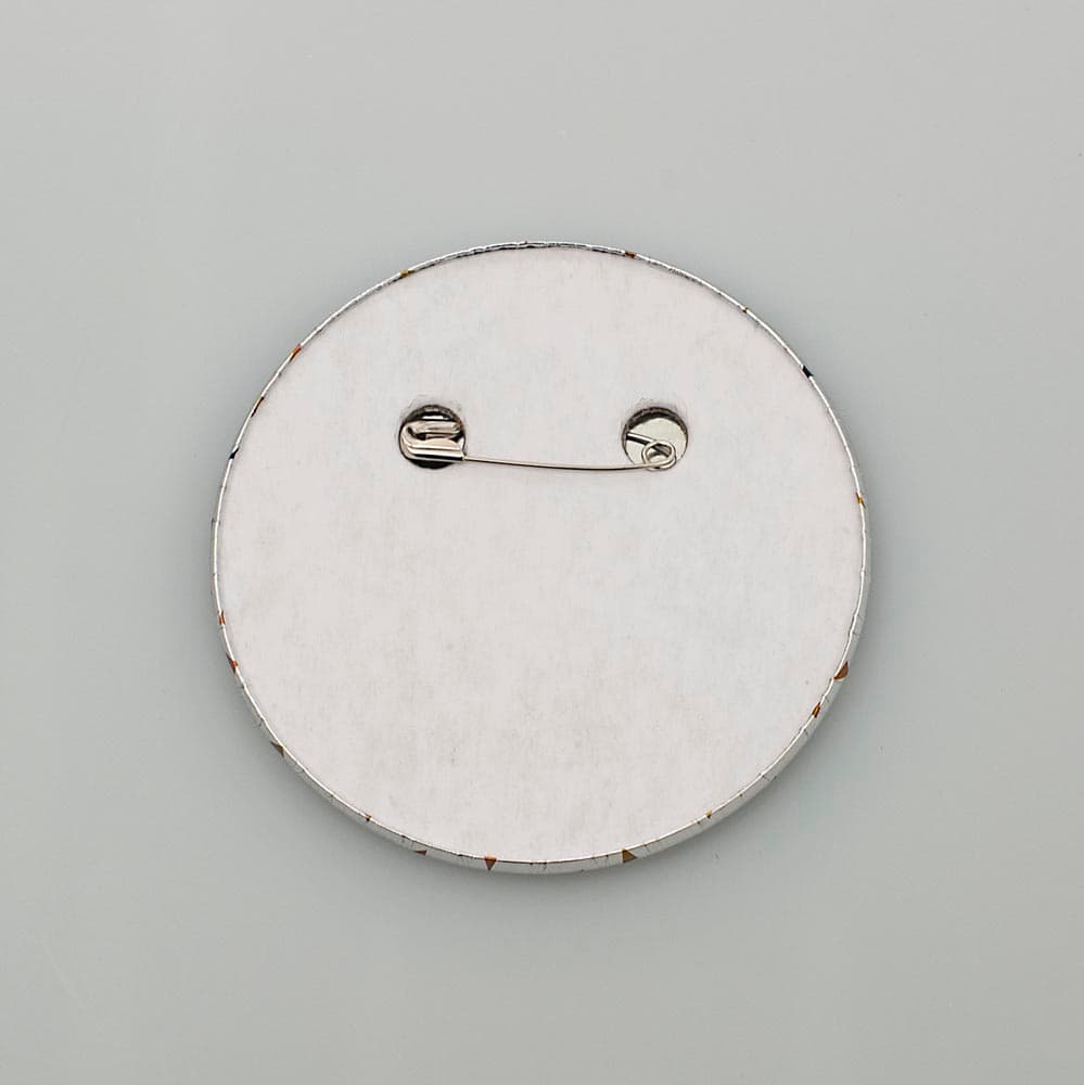 A ROUND BADGE WITH 'I'M 60' PRINTED ON IT. THE BADGE IS MADE OF TIN AND IT IS MOUNTED ONTO 1.5 MMM THICK LINED GREYBOARD ATTACHED TO WHICH IS A STAINLESS STEEL SAFETY PIN SO BADGE CAN BE ATTACHED TO CLOTHING. THE FRONT HAS A COVER OF POLYETHYLENE FOIL WITH METALLIC PAINT APPLIED TO IT.