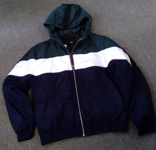 A WOVEN WINDJACKET FOR UNISEX. 
DESIGNED TO COVER THE UPPER PART OF THE BODY FROM THE NECK TO JUST BELOW THE WAIST. WITH COMPLETE FRONT OPENING FASTENED BY A ZIP. WITH ELASTICATED TIGHTENING AT THE BOTTOM OF THE GARMENT. WITH LONG SLEEVES AND ELASTICATED SLEEVE ENDS. WITH TWO SIDE OUTER POCKETS. ROUND NECK HOOD WITH DRAW-CORD TIGHTENING.  PADDED WITH LINING. WITH INSIDE BREAST POCKET.
3 DIFFERENT COLOURED STRIPS ACCROSS THE BODY FROM TOP TO BOTTOM, GREEN, WHITE AND BLUE.
MADE FROM 100 PER CENT POLYESTER.