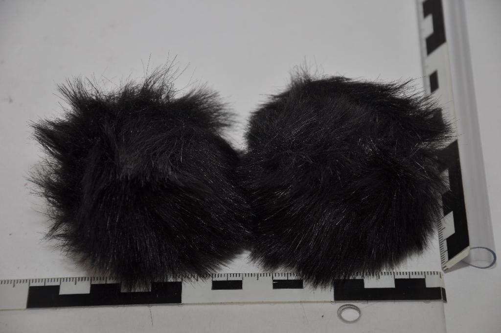 A termék fényes, fekete színű, kb. 7 cm átmérőjű, gömb alakú pompon. A minta bélése fehér színű textilszálakból áll, mely egy fekete színű kötött/hurkolt anyaggal van bevonva, erre az anyagra vannak a kb. 2,5 cm hosszú fekete színű szálak rácsomózva. A minta egyik oldalán fehér színű, kör alakú anyag található, melyre egy fémből készült klipsz van felvarrva, mely segítségével a cipőre erősíthető a pompon.
A pompon cipő díszítő elemként használatos.
A minta összeerősített rövid szálai: textilanyagból (poliakrilnitrilből), bélés anyaga: textilanyagból (polipropilénből) és a klipsz: nem nemesfémből áll.