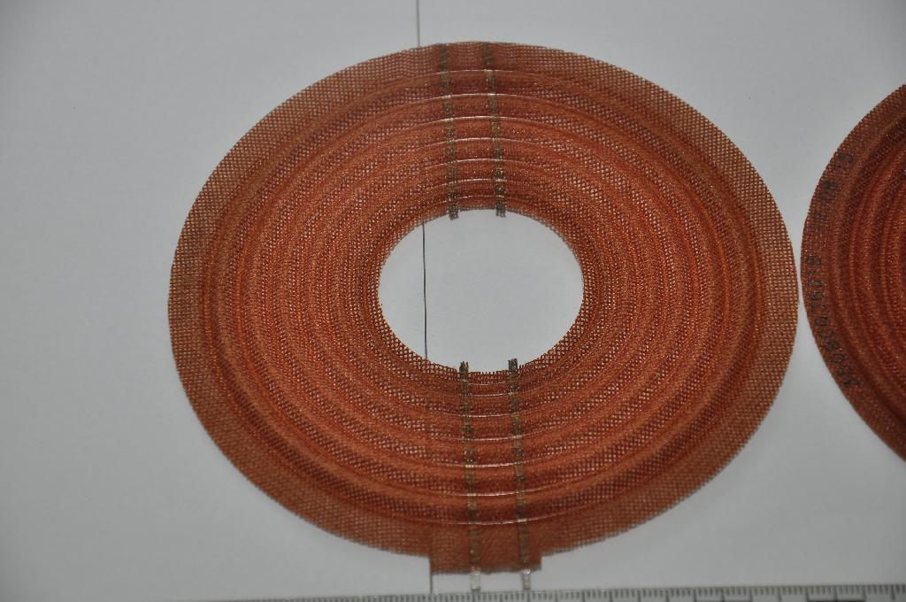 A termék barna színű, hajlékony, gyűrű alakú textil mintázatú hangszóró pille. 0,4 mm vastagságú, 121,7 mm külső átmérőjű, 40,1 mm belső átmérőjű textil lap, amely koncentrikusan, hullámszerűen hajlított. A szövetbe 4 x 3 db, párhuzamos fémsodrony van beleágyazva, végük forrasztott, elektromosan nem szigetelt.
A termék személygépjárművekbe építendő hangszórókban használatos, a hangszóró alsó központosító és rugózó alkatrésze. A pille adja a hangszóró stabilitását, a membránt központosan tartja, a lengőtekercset a légrésbe tájolja. A textil rész látja el a rezgéscsillapítást és a központosítást, a rézszál vezeti ki a kosárra az áramot a lengőtekercs irányából.
A termék egyik része Conex (meta-aramid rost) alapanyagú, aramid szálakból szőtt szövet, a nem szigetelt rézkábelek/fémszálak főkomponensei réz és ezüst, a fémszálak végén lévő forraszanyag ón.  A rézszálon lévő ezüstbevonat oldatba való bemerítés útján kerül felvitelre.