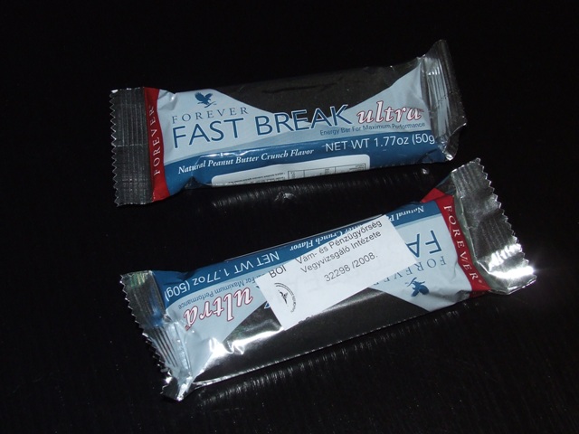Forever Living Fast Break Ultra csokoládé bevonatú energia szelet. A minta eredeti kiszerelésű, ezüst/kék alapszínű fólia csomagolásban érkezett, bontatlan állapotban. A kiegészítő magyar nyelvű címkén az alábbiak olvashatók: Forever Fast Break Ultra Bar (268), nettó tömeg, vitaminokban és ásványi anyagokban gazdag energiaszelet mogyoróvajjal és mogyoró darabkákkal, összetétel, tápértékadatok, származási hely: USA, kizárólagos forgalmazó: Forever Living Products. Érzékszervi vizsgálat: kb. 9 cm hosszú, 3 cm széles, 1,7 cm magas, barna színű csokoládéval teljesen bevont szelet, belsejében mustársárga színű, földimogyoró illatú és ízű, földimogyoró darabokat is tartalmazó töltelékkel. Laboratóriumi vizsgálatok: Cukortartalom (HPLC): szacharóz 8,9 m/m%, fruktóz 4,4 m/m%, glükóz 8,0 m/m%, laktóz nem mutatható ki. Tejzsírtartalom (GC): < 1 m/m%, keményítő-tartalom: 7 m/m%, tejfehérje-tartalom < 2,5 m/m%, kakaótartalom (HPLC): 1,6 m/m%. Meursing kód: 7001. - tejzsír: >= 0 < 1,5 - tejfehérje: >= 0 < 2,5 - keményítő/glükóz: >= 0 < 5 - szacharóz/invertcukor/izoglükóz: >= 5 < 30. Az elvégzett érzékszervi és laboratóriumi vizsgálatok, valamint a csatolt összetételre vonatkozó Nyilatkozat alapján a minta csokoládéval teljesen bevont, töltött szeletáru.