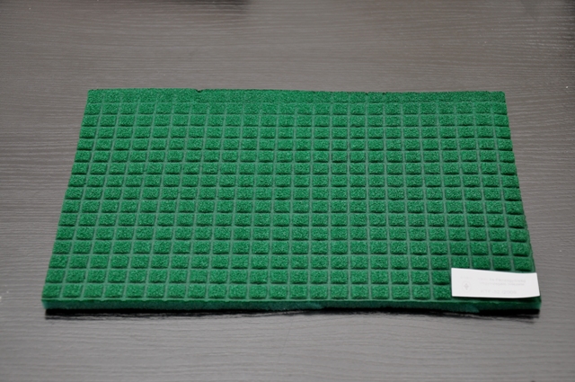 Szivacslap. A mintán végzett vizsgálatok eredménye: Érzékszervi vizsgálat: a minta 30,5 x 20,2 x 0,9 cm-es világoszöld színű műanyag szivacslap, melynek egyik felén mártott, sötétzöld színű bevonat található. A bevonatos oldalán négyzetrácsban, 12 milliméterenként kb. 2 mm széles és 1 mm mély barázdák találhatók. FT-IR vizsgálat: A minta szivacsos alapjának anyaga FT-IR alapján poliuretán. A bevonat anyaga feltehetően poliészter gyanta. Mikroszkópos vizsgálat: a bevonat alatt a szivacs eredeti szerkezete jól látható. Az elvégzett vizsgálatok és a benyújtott nyilatkozatok alapján a minta porózus poliuretán lap, amelynek egyik oldala poliészter gyantával van bevonva. A mintában a poliuretán mennyisége a nagyobb.