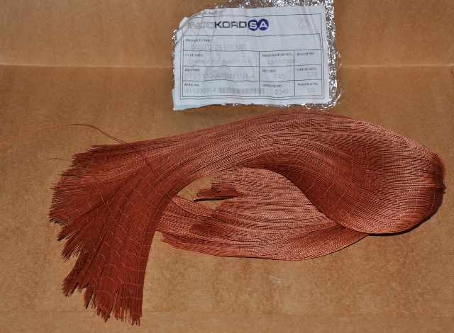 Kerékköpeny kordszövet magas szakítószilárdságú poliamid fonalból gumival impregnálva (nylon szövet).
Csomagolás: A minta drapp színű, átlátszó műanyag zsákba kötve érkezett a laboratóriumba vizsgálatra. Vizsgálati eredmények: Érzékszervi vizsgálat: A minta speciális célra kialakított, barna színű, egyik oldalán eredeti, széllel, visszaforduló vetülékfonalakkal, másik három oldalán vágott, kerékköpeny kordszövet, ahol a láncfonalakat egymástól 1,6 cm távolságban barna színű vetülékfonalak fogják össze. Beküldött minta méretei: szélesség: 106 cm, hosszúság: 68–70 cm. Kelmeképzés: szőtt, vászonkötés, a szövet felületén szabad szemmel jól látható, drapp színű bevonat van. Nyersanyag összetétel (MSZ 13560-2:1989): láncfonal: poliamid; vetülékfonal: pamut és viszkóz szálkeverék. Négyzetmétertömeg (légszáraz állapot): 231,20 g/m2. Nyersanyag összetétel mennyiségi meghatározása kézi szétválasztás módszerével (25/2005. (IV.29.) GKM rendelet): poliamid szálak aránya: 99,4 %, pamut és viszkóz szálak aránya: 0,6 %. Bevonat mennyiségének meghatározása kémiai szétválasztással (házi módszer): bevonat aránya (a  minta teljes tömegére számítva): 5,77 m/m%. FT-IR vizsgálat (bevonat minőségi meghatározása): sztirol/butadién/poliizoprén/rezorcin/formaldehid kopolimer. Bevonat latex tartalmának mennyiségi meghatározása FT-IR vizsgálattal: Sztirol/butadién tartalom: 47±3 m/m%, Poliizoprén tartalom: 28±2 m/m%. A minta kerékköpeny kordszövet 99 % poliamid fonalból és 1% pamut és viszkóz szálkeverékből, szabad szemmel jól látható módon butadién/sztirol/poliizoprén/rezorcin/formaldehid gyantával impregnálva. A bevonat latex tartalma: 75±5 m/m%. A csatolt dokumentumok alapján a kétágú láncfonalak szakítószilárdsága: 69,673 cN/tex, a termék nagy szakítószilárdságú poliamid fonalból készült.
