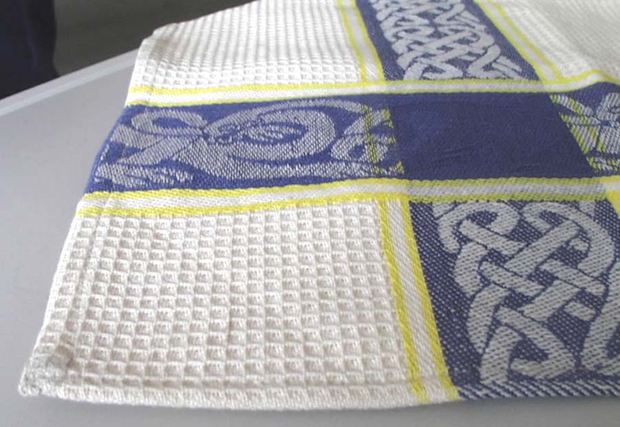 TEA TOWEL OF 100% COTTON, HEMMED ON ALL SIDES.  THE TEA TOWEL IS PRINTED WITH A CELTIC-TYPE DESIGN.