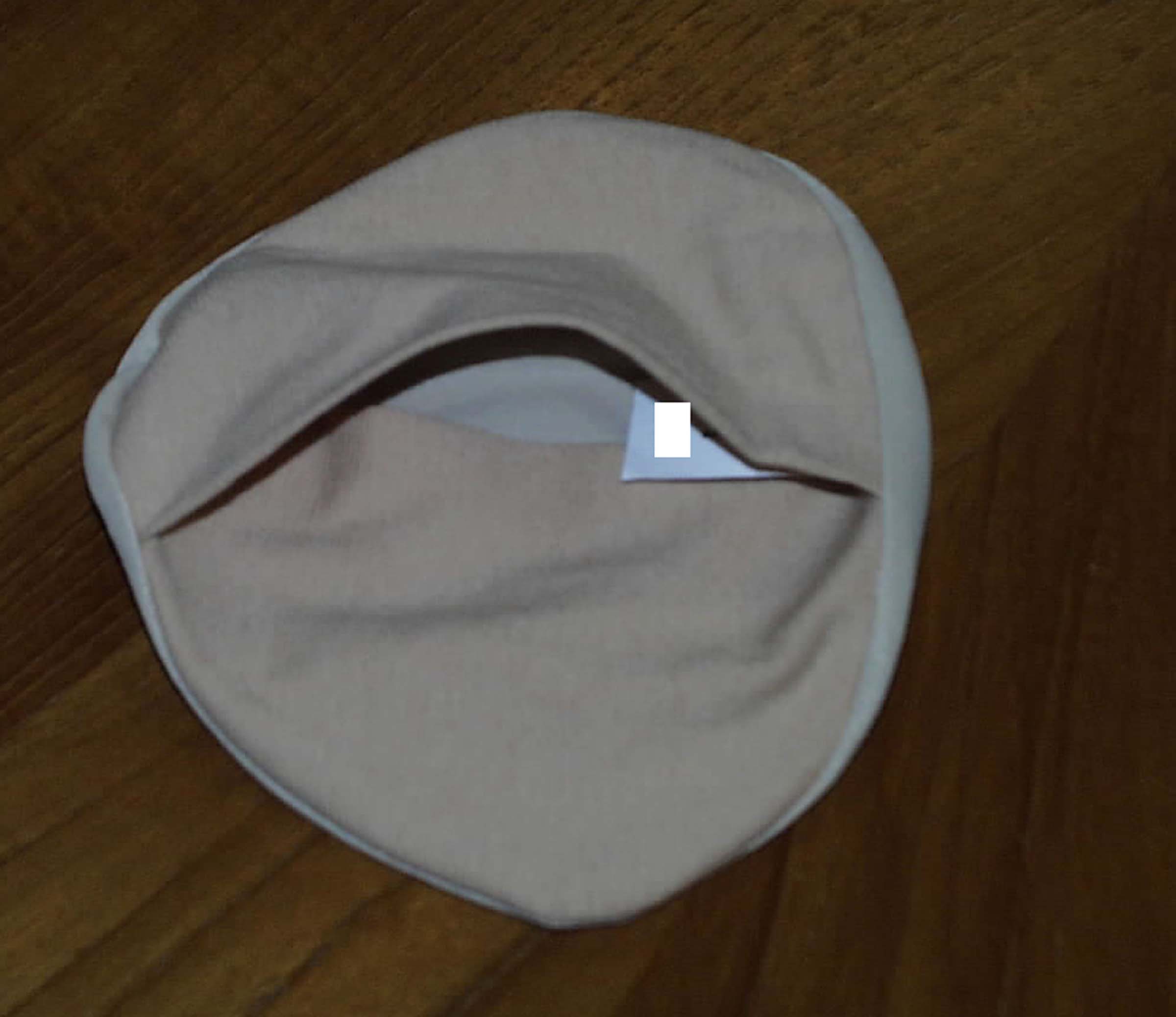 A KNITTED TEXTILE COVER USED TO HOLD A SILICONE BREAST PROSTHESIS.  THE COVER IS ALMOST CIRCULAR IN SHAPE, THE TOP IS COMPOSED OF 80% NYLON AND 20% SPANDEX AND IS HEMMED ALL AROUND TO A BASE OF 95% COTTON AND 5% SPANDEX.  THE BASE HAS A FULL OPENING TO ALLOW THE PROSTHESIS TO BE INSERTED AND REMOVED AND BOTH SIDES OVERLAP TO KEEP THE PROSTHESIS ENCLOSED.