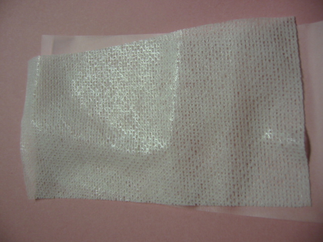 A NON-WOVEN 50% RAYON AND 50% POLYESTER FABRIC OF MAN-MADE FILAMENT COATED WITH A SILICONE ADHESIVE ON BOTH SIDES. THE ADHESIVE LAYER IS COVERED BY A RELEASE PAPER WHICH PEELS FREELY FROM THE ADHESIVE COATING. IT COMES IN ROLLS AND IS USED IN THE MANUFACTURE OF DRESSINGS FOR WOUNDS. IT WEIGHS LESS THAN 25G/M2