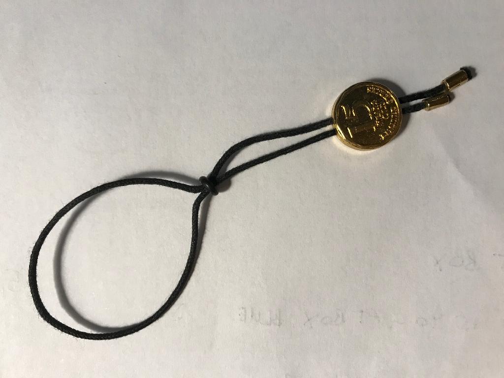 METAL PLATE ON A COTTON CORD. IT IS PERMANENTLY FIXED TO A BOTTLE AND IS FOR ADVERTISING AND DECORATIVE PURPOSES.  THE PLATE IS A ZINC ALLOY. THE DIAMETER IS 15MM, 5MM THICKNESS. THE ROPE IS BLACK COTTON WITH A DIAMETER OF 1MM AND LENGTH 240MM.