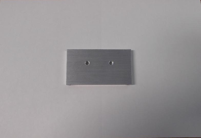 HEAT SINK / EXCHANGER. IT IS A RECTANGULAR METAL PLATE WITH TWO THREADED HOLES AND TWO UNTHREADED HOLES.
IT REDUCES HEAT FROM AN ELECTRICAL COMPONENT AND IS SHAPED FOR USE IN A POWER CONVERTER. THE THREADED HOLES ARE IN A SPECIFIC LOCATION SO THAT THE ARTICLE CAN BE PRECISELY ATTACHED TO THE PRINTED CIRCUIT BOARD. THE UNTHREADED HOLES ARE ALSO IN A SPECIFIC LOCATION AND CAN ACCEPT SELF-TAPPING SCREWS WHICH HELPS TO STABILISE THE ARTICLE ON THE PCB.
IT IS MADE OF COPPER WITH AN ALUMINIUM COATING.
