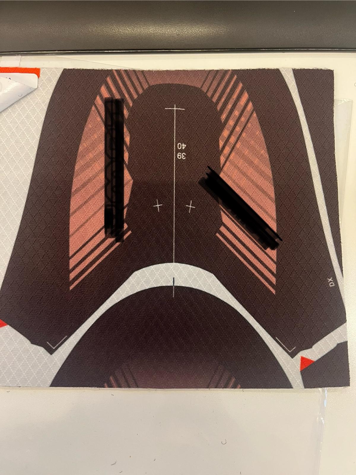 Tessuto indemagliabile a base di poliestere, presentato in rotoli, destinato alla realizzazione di tomaie per calzature. Il prodotto si presenta con disegno stampato sul lato esterno, raffigurante la sagoma della tomaia secondo specifiche del cliente, mentre il lato interno è a tinta unita nera e si presenta soffice al tatto.
Il materiale è costituito da tre strati accoppiati, uniti mediante una resina traspirante:
due strati tessili a maglia, di cui uno interno a contatto con il piede, con funzione di comfort e traspirabilità;
uno strato intermedio in tessuto non tessuto (TNT), con funzione strutturale e di rinforzo.
Il tessuto risulta traspirante, grazie alla composizione in fibre sintetiche (poliestere) e alla natura della resina di accoppiamento.
Il lato esterno è stampato industrialmente con il disegno della tomaia, mentre il lato interno, uniforme e privo di stampa, presenta una mano morbida.
Le tomaie ricavate dal tessuto vengono direttamente montate su una suola, senza necessità di ulteriori trasformazioni sostanziali del materiale, per ottenere la calzatura finita.
Dall’esame del campione emerge pertanto un foglio di tessuto multistrato, con struttura composita, comprendente strati a maglia e uno strato in tessuto non tessuto, accoppiati in modo permanente, recante stampa funzionale alla sagomatura delle tomaie.