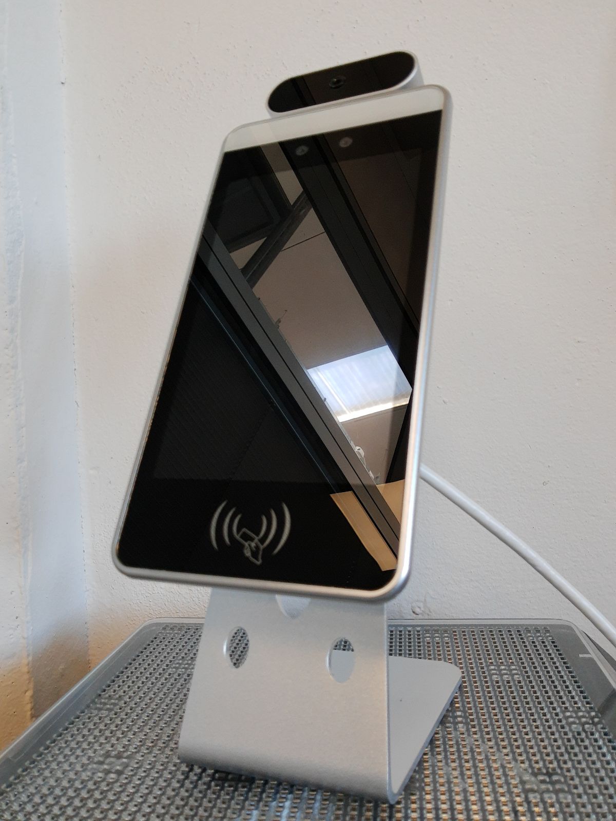 Termocamera per il rilevamento della temperatura.
Per dichiarazione di parte, l’articolo  è un dispositivo/terminale statico verticale, con una struttura in acciaio, utilizzato per la misurazione della temperatura corporea senza contatto ad una distanza di 0.5-2 metri. Il terminale è dotato di uno schermo LCD HD, un sensore di temperatura corporea ad infrarossi, una fotocamera ad alta risoluzione, due LED bianchi per l’illuminazione automatica del volto in caso di scarsa illuminazione ambientale, LED verdi/rossi di segnalazione, un altoparlante, un sistema operativo open source e la relativa applicazione per il riconoscimento della temperatura pre-installata e configurata nello startup ad ogni avvio, una scheda su cui sono integrati in modalità non intercambiabile: una CPU, RAM, una memoria EMMC da 16 GB, un modulo WiFi, un modulo 4G e Bluetooth. L’articolo è fornito con un gruppo di cablaggi con le connettività ethernet, RS232, USB ed alimentazione. La misurazione della temperatura avviene nel viso tra il ponte del naso, viso, condotti lacrimali e fronte dei volti riconosciuti nello spazio inquadrato da fotocamera e sensore. Il dispositivo è fornito di uno specifico  software che permette di riconoscere se davanti ai sensori è posizionato un oggetto inanimato o una persona e riconoscere se l’utente ha indossato correttamente una mascherina  nel contesto di controllo della diffusione di virus e malattie infettive. Le temperature rilevate  vengono mostrate sullo schermo, con un messaggio acustico e, tramite relativi LED di segnalazione (verde/rosso), viene segnalato facilmente all’utente se tutte le condizioni (temperatura e presenza della mascherina facciale) sono rispettate.