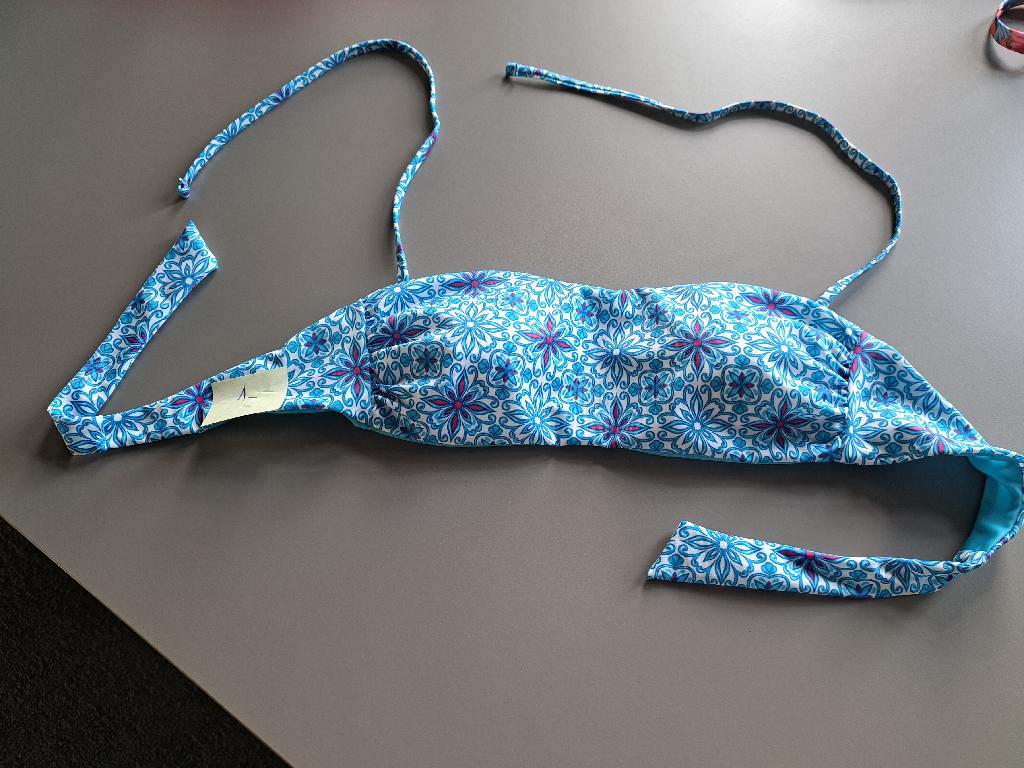 Reggiseno, cosiddetto top bikini da donna a fascia, realizzato in tessuto foderato a maglia di fibre sintetiche; ha  lacci verticali  da allacciare dietro al collo e fasce  orizzontali di tessuto da annodare sulla schiena. Il reggiseno è dotato di coppe sagomate all'interno.