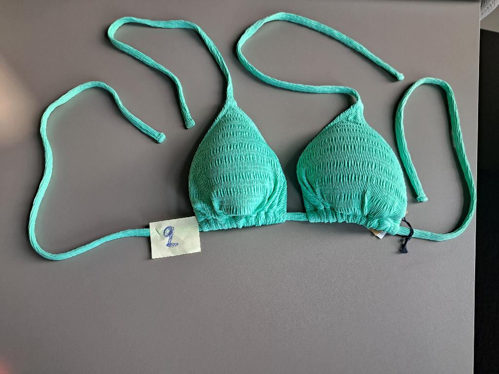 Reggiseno, cosiddetto top bikini da donna, realizzato in tessuto foderato a maglia di fibre sintetiche; ha laccetti da annodare dietro al collo e sulla schiena. Il reggiseno è dotato di coppe sagomate all'interno.