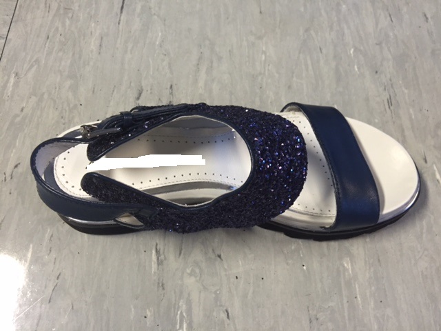 SANDALO DA DONNA CON TOMAIA FORMATA DA STRISCE DI DIVERSA LARGHEZZA, UNA IN PELLE E L’ALTRA IN MATERIA PLASTICA SOTTO FORMA DI GLITTER SUPPORTATO DA MATERIA TESSILE; ENTRAMBI I MATERIALI SONO DI COLORE BLU. LA CALZATURA E’ MUNITA DI UN CINTURINO REGOLABILE PASSANTE DIETRO IL TALLONE E DOTATO DI UNA FIBBIA IN METALLO. LA SUOLA ESTERNA, APPLICATA ALLA TOMAIA PER INCOLLAGGIO, E’ COSTITUITA DA GOMMA E PRESENTA EVIDENTI RILIEVI ANTISCIVOLO SU TUTTA LA LUNGHEZZA. LA TOMAIA E’ COSTITUITA PREVALENTEMENTE DAL GLITTER IN PLASTICA ED IN MISURA MINORE DA PELLE. ENTRAMBI DI COLORE BLU. LA CALZATURA NON PRESENTA TACCO MA E’ COSTITUITA DA UN’UNICA PIATTAFORMA LA CUI ALTEZZA MASSIMA SUPERA I TRE CM. L’INTERNO DELLA CALZATURA E L’INTERSUOLA  SONO FODERATI DI PELLE. LA SUOLA INTERNA NON RAGGIUNGE I 24 CM DI LUNGHEZZA.