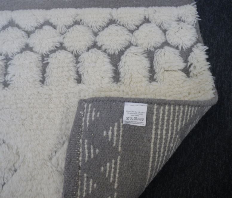 Taisnstūra formas austs paklājs no vilnas (85 %) un kokvilnas (15 %). Izmēri 70 x 140 cm. Šaurākās malas ir nolocītas un nošūtas. Paklājs ir ar šūtām plūksnām.