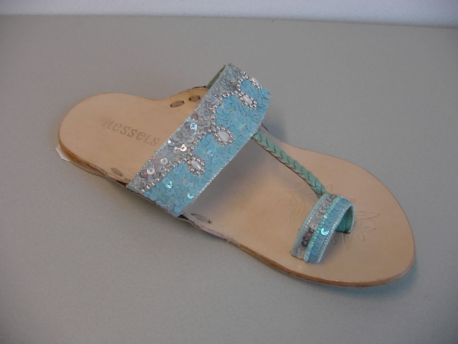 Een damesslipper met een bovendeel van textiel en een buitenzool van leder. De slipper heeft aan beide zijden, ter hoogte van de voetholte, twee ronde uitstekende delen leder. Het bovendeel bestaat uit een band die dwars over de wreef loopt en tussen de uitstekende delen leder is vastgemaakt en aan de voorzijde over een band die dwars over de grote teen loopt. Beide banden hebben applicaties in de vorm van sierstiksels, kralen en pailletten. Aan de band over de wreef is een lederen gevlochten band bevestigd die naast de band over de grote teen in de zool is bevestigd. De slipper heeft een rubberen hak met een dikte van ongeveer 3 mm.