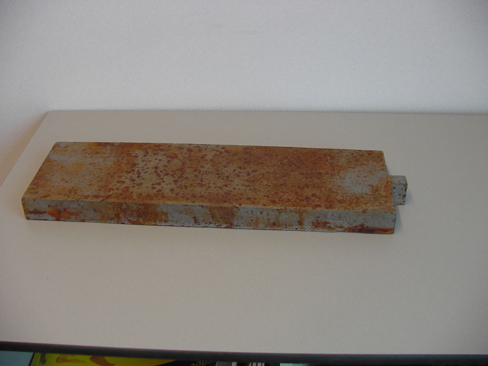 Contragewicht van gietijzer, met de afmetingen (L x B x H) van ongeveer 34 x 10 x 2,5 cm, met een kleine uitstulping van ongeveer 1,5 x 1,4 cm aan één zijde. Het gestampte artikel wordt -volgens opgaaf- gebruikt in de meubelindustrie om ladenblokken niet te laten kantelen.