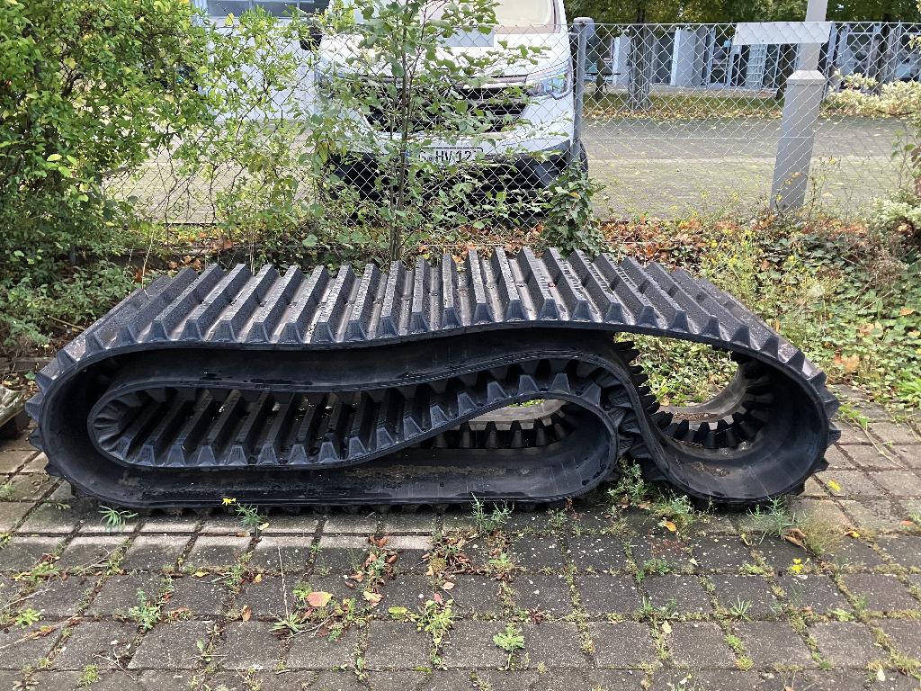 Een rupsband (aandrijfband) met -volgens opgave- onder andere de volgende kenmerken en eigenschappen:
- ontworpen voor gebruik met zelfrijdende grondverzetmachines, zoals graafmachines, rupsvoertuigen, kiepwagens en rupsladers;
- geheel en al vervaardigd van niet-geharde gevulkaniseerde rubber;
- in de vorm van een eindeloze band;
- aan de loopvlakzijde voorzien van dwarsbalken, die het loopvlak vormen;
- aan de bevestigingszijde voorzien van tanden.