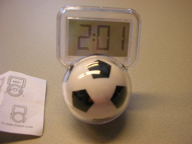 Een elektrisch werkend digitaal bureauklokje met horloge-uurwerk in een behuizing van kunststof, in de vorm van een voetbal, voorzien van de volgende kenmerken:
- een LCD scherm met de afmetingen 3,7 x 2,3 cm, voor weergave van 
  tijd en datum;
- een afsluitbare ruimte voor één knoopcelbatterij;
- twee bedieningsknoppen aan de achterzijde;
- met de afmetingen 7,5 x 5 x 5cm.
Het artikel is opgemaakt voor de verkoop in het klein en wordt tezamen aangeboden met een gebruiksaanwijzing, verpakt in een kartonnen doosje.