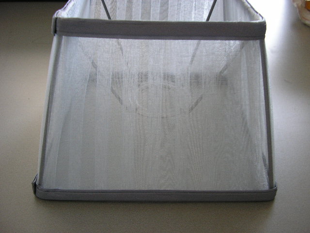 Een vierkante lampenkap, taps toelopend, met een metalen frame en een kapbekleding van textiel. De kap heeft aan de bovenzijde afmetingen van ongeveer 140 x 140 mm, aan de onderzijde afmetingen van ongeveer 200 x 200 mm en een hoogte van ongeveer 138 mm. Aan de binnenzijde is een voorziening van onedel metaal aangebracht waarmee de lampenkap op de lampvoet geplaatst kan worden.