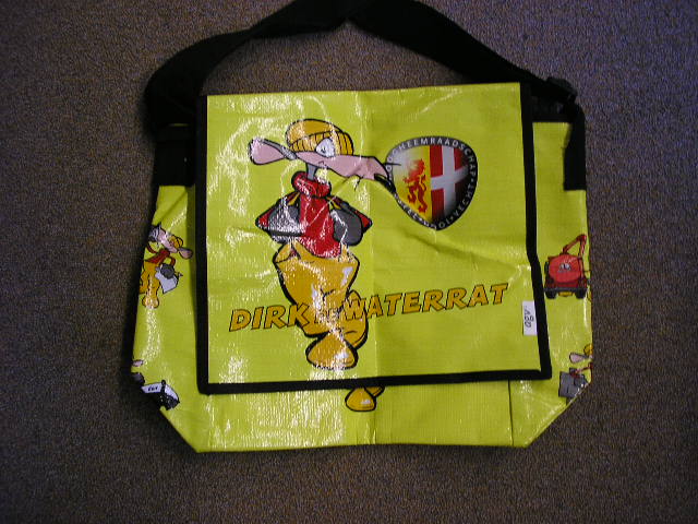Een schoudertas met een buitenkant van kunststof in vellen voorzien van een verstelbare schouderriem van textiel. De tas is voorzien van een overslag die met klittenband wordt gesloten en heeft afmetingen van ongeveer 31x31x13 cm (lxbxd).