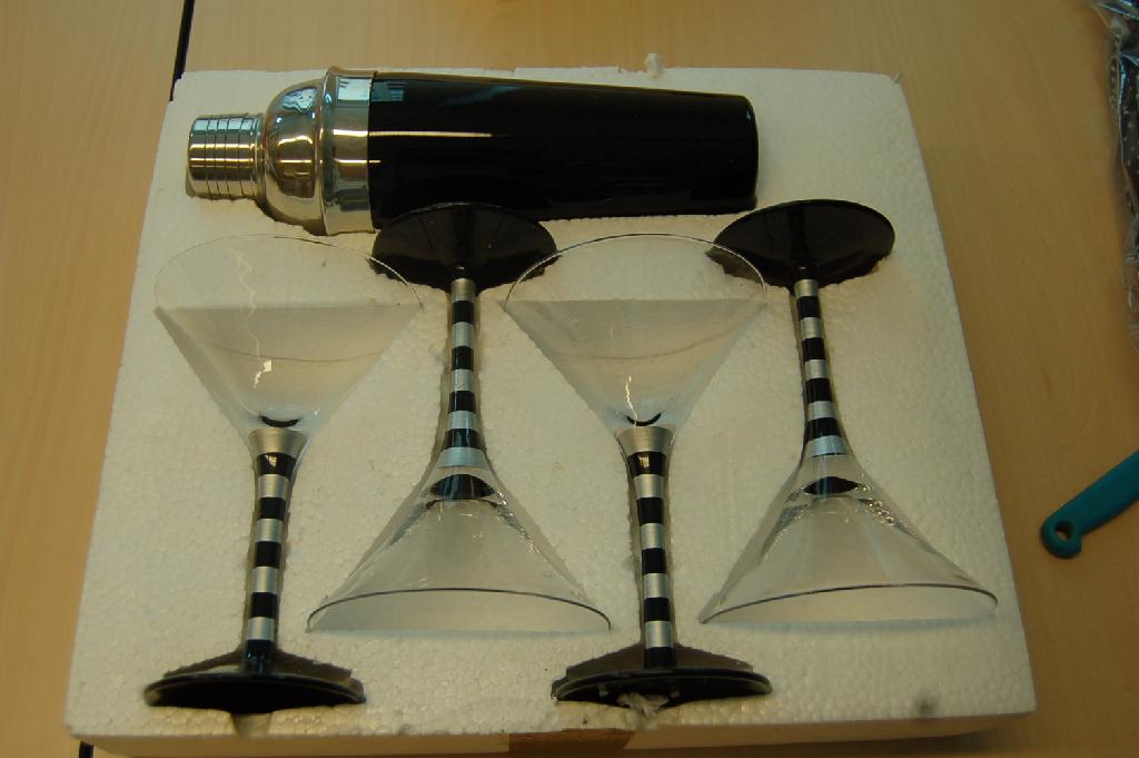 Cocktailset, bestaande uit een shaker van onedel metaal met glas en vier mechanisch vervaardigde glazen op een voet. De shaker heeft een hoogte van ongeveer 27,5 cm, de glazen hebben een hoogte van ongeveer 18 cm. Het geheel is opgemaakt voor de verkoop in het klein en kan worden aangemerkt als een assortiment waarbij het wezenlijk karakter wordt bepaald door de glazen.