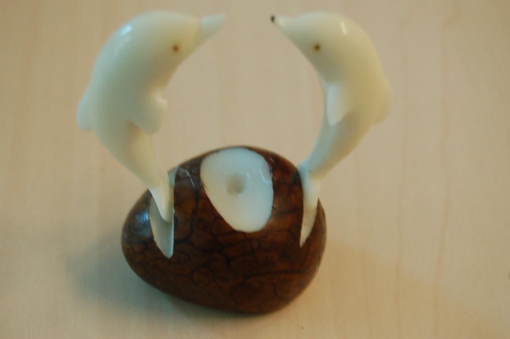 Een gedroogde noot van de tagua palm met drie uitsparingen waarin in de buitenste uitsparingen dolfijnen van hetzelfde materiaal zijn geplaatst.
