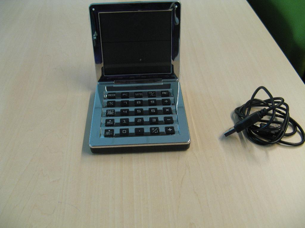 Een samengesteld apparaat geplaatst in een voorgevormde behuizing van kunststof en onedel metaal, bestaande uit een rekenmachine, een klokje en een cijfer-toetsenbord voor een automatische gegevensverwerkende machine (computer).
Het apparaat heeft ondermeer de volgende kenmerken:
- opklapbaar deksel;
- klokje met datum en tijdsaanduiding;
- met LCD scherm;
- toetsenbord voorzien van bedieningstoetsen;
- afmetingen behuizing van ongeveer 9,5x9,5x1,8 cm;
- voorzien van USB aansluiting en kabel.
Het wezenlijk karakter van het samengestelde apparaat wordt bepaald door de rekenmachine.