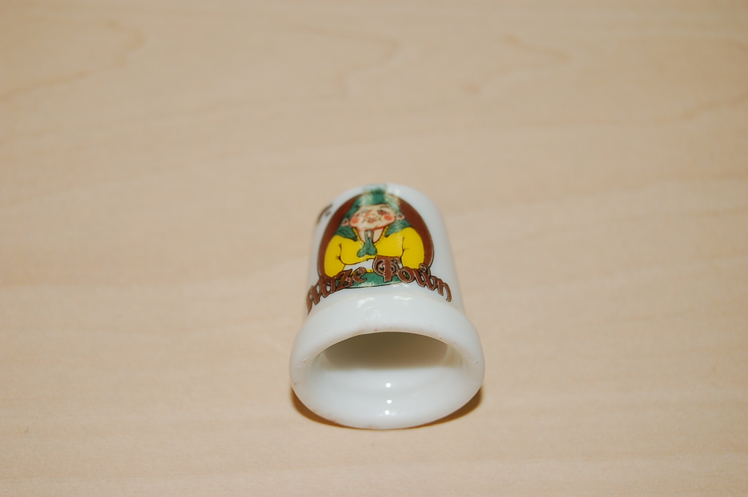 Een vingerhoedje vervaardigd van porselein voorzien van een decoratieve print. Het vingerhoedje heeft een diameter en een hoogte van ongeveer 25 mm. De vingerhoed is verpakt in een voorgevormd kunststof houder in een kunststof doosje, gereed voor de verkoop in het klein.