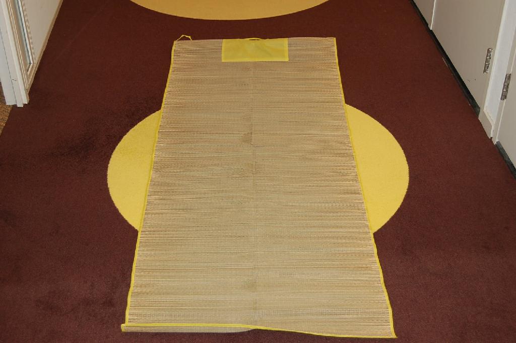 Een strandmat vervaardigd van vlechtstoffen van stro in strippen met een breedte van ongeveer 1,2 mm, samengebonden met een textielgaren. De mat bestaat uit vlechtstoffen die rondom zijn afgebiesd met een strookje synthetische textielvezels van polyester. Het artikel heeft afmetingen van ongeveer 180 x 70 cm. Het wezenlijk karakter van het geheel wordt bepaald door het vlechtwerk bedoeld in hoofdstuk 46.