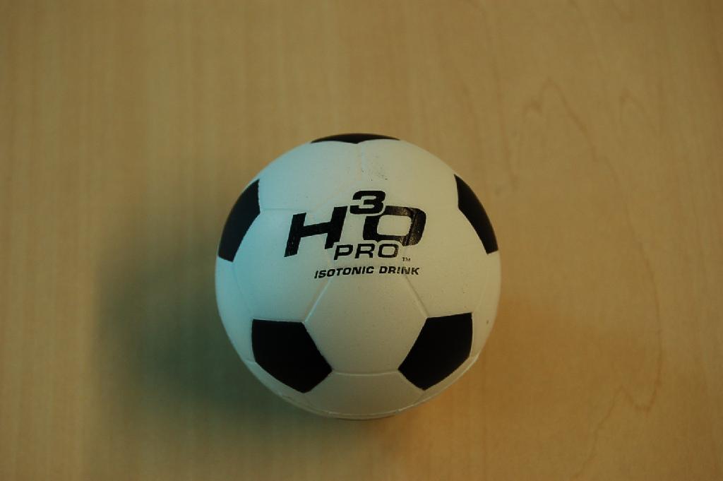 Een zogenaamde anti stress bal van zachte kunststof in de vorm van een voetbal met een diameter van ongeveer 6 cm en voorzien van een bedrijfslogo.