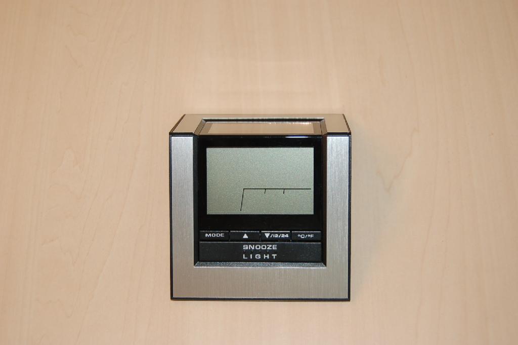 Een digitaal bureauklokje voorzien van een ander uurwerk dan een horloge-uurwerk, heeft ondermeer de volgende kenmerken: 
- afmetingen (LxBxH) ongeveer 110X90X40 mm; 
- afmetingen LCD ongeveer 55x35mm; 
- met datum-, tijd-, dag- en temperatuur aanduiding; 
- met diverse bedieningknopjes onder het LCD-scherm, zijkant en onderzijde; 
- aan de onderzijde voorzien van een compartiment voor 3 AAA batterijen.
Het klokje kan functioneren op 3 AAA batterijen of op zonenergie, waarvoor zonnecellen aan de achterzijde zijn aangebracht. Het wezenlijk karakter van het artikel wordt bepaald door de bureauklok met wekkerfunctie. Het klokje wordt aangeboden in een kartonnen verpakking tezamen met een instructiefolder en is gereed voor de verkoop in het klein.