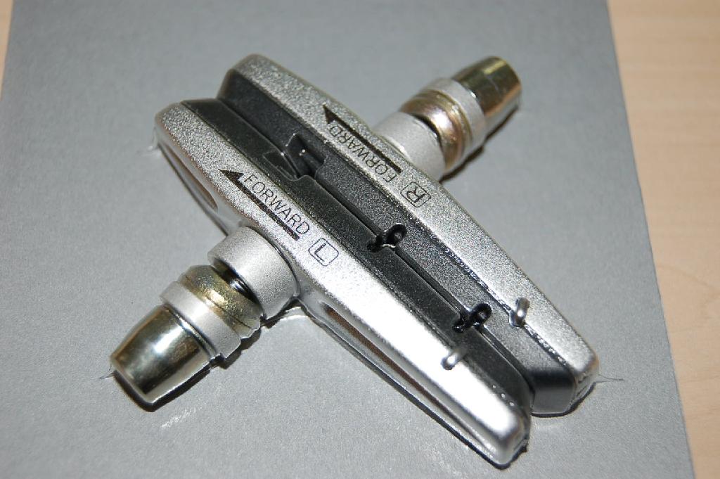 Een remschoen voor een niet gemotoriseerd rijwiel, bestaande uit een metalen houder (cartridge) met een - volgens opgave- rubberen remblok en een schroef met sluitringen voor het bevestigen. De remschoen is te onderkennen als een deel van een rem voor een fiets van GN 8712.